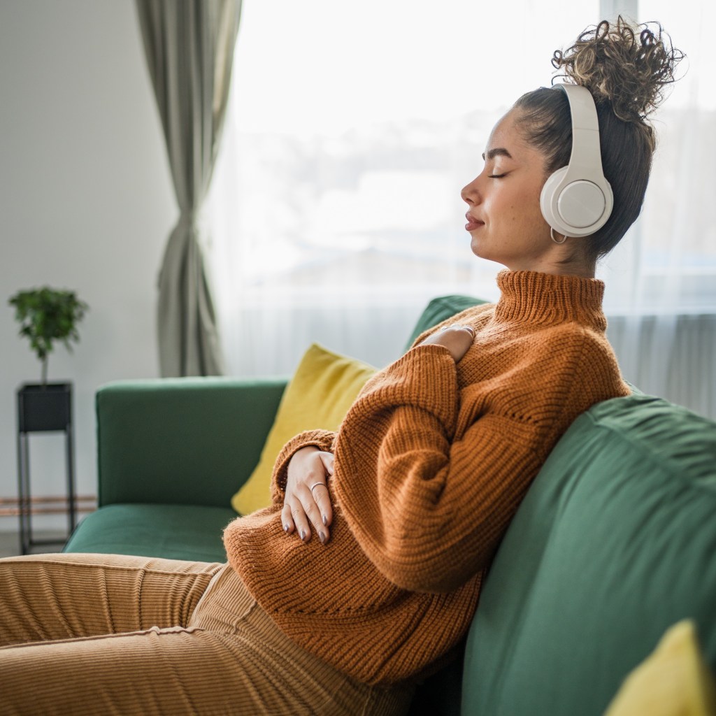 image of person listening to a meditation via headphones, eyes closed, relaxed with hands on heart and abdomen
