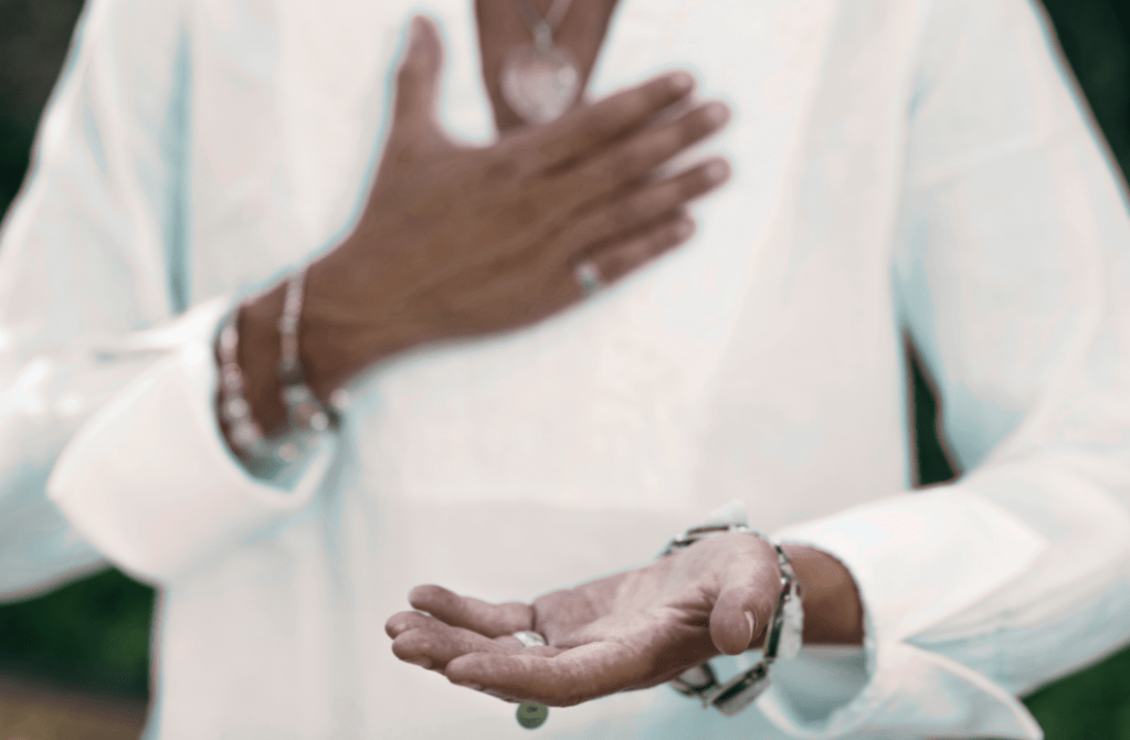 Image of a person with a hand over their heart and the other in front, palm facing up in offering.